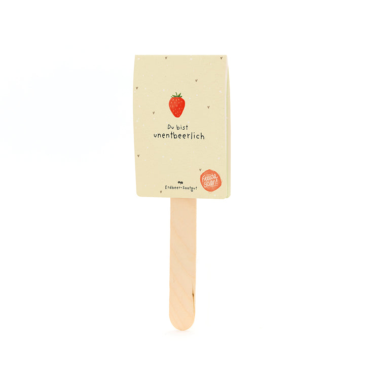 Holzstab mit einem Etikett, das eine Erdbeere und den Text „Du bist unentbeerlich“ sowie „Erdbeer-Saatgut“ zeigt.