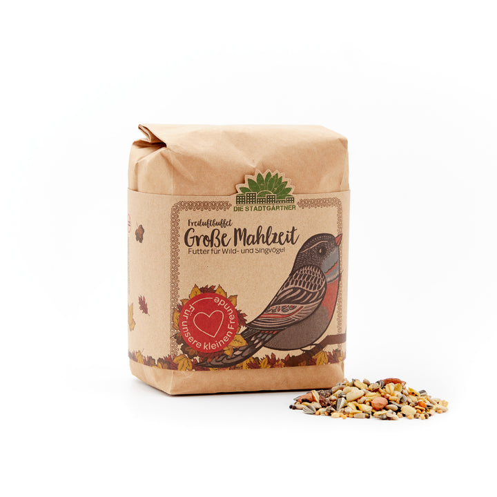 Papiertüte mit Vogelzeichnung und der Aufschrift "Große Mahlzeit – Futter für Wild- und Singvögel" neben einer kleinen Portion Vogelfutter auf weißem Hintergrund.