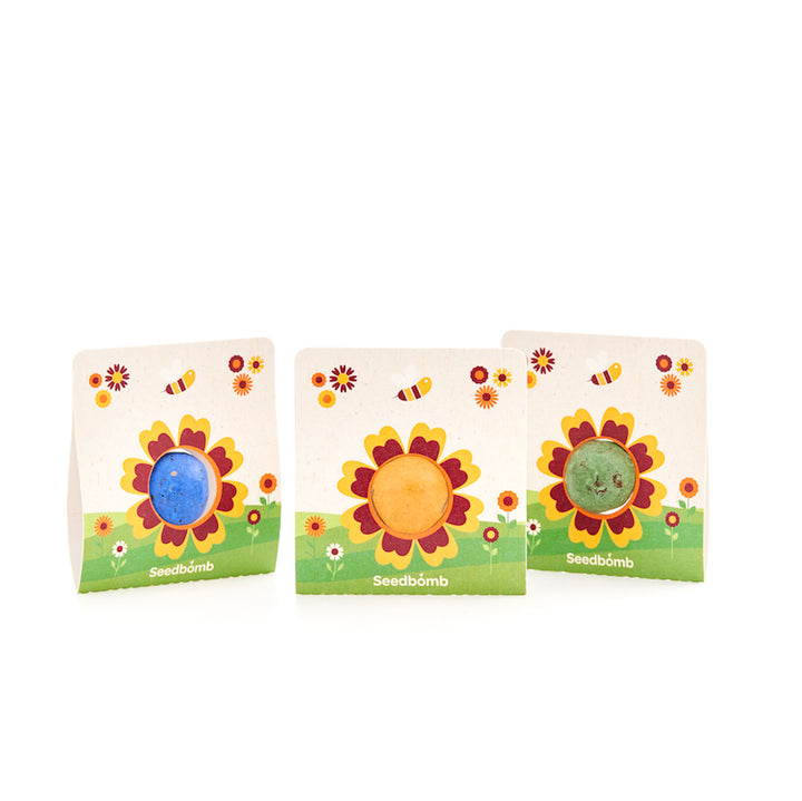 Drei bunte Seedbombs in Verpackungen mit Sonnenblumen- und Bienenmotiven auf weißem Hintergrund.