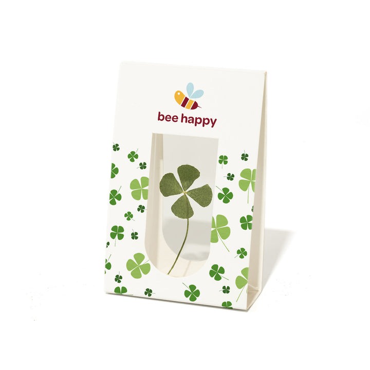 Papiertüte mit vierblättrigem Kleeblatt und dem Text "bee happy" sowie einer Bienenillustration.
