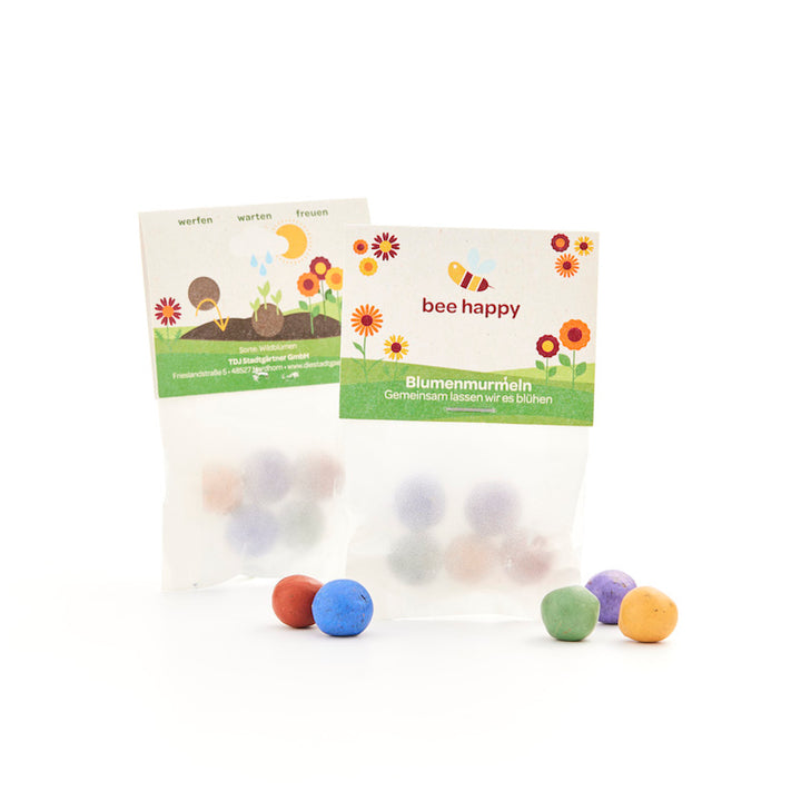 Zwei Tütchen mit bunten Blumenmurmeln, auf der Verpackung steht „bee happy“ und sie ist mit Blumen und einer Biene illustriert.