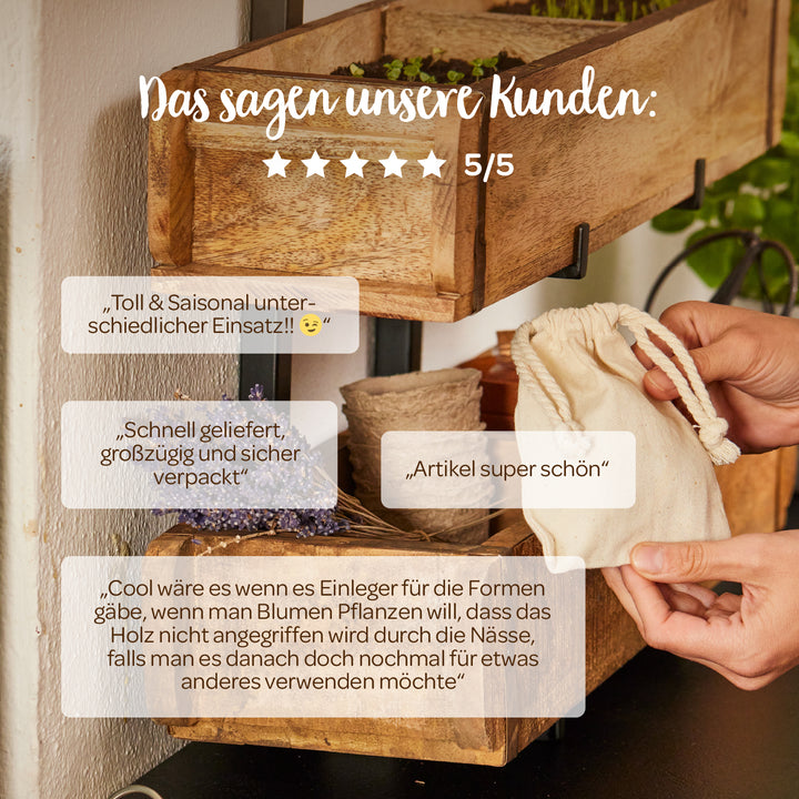 Ein Bild von einer hölzernen Pflanzenbox mit verschiedenen Kundenbewertungen auf Deutsch, eine Hand hält einen kleinen Stoffbeutel, dekorative Blumen und Pflanzen im Hintergrund.