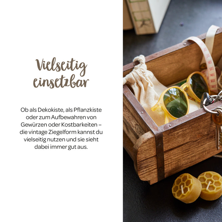 Holzkiste im Vintage-Stil mit Sonnenbrille, Schlüssel, Stoffbeutel und Maßband auf einem Tisch, daneben zwei gelbe Wachsstücke.