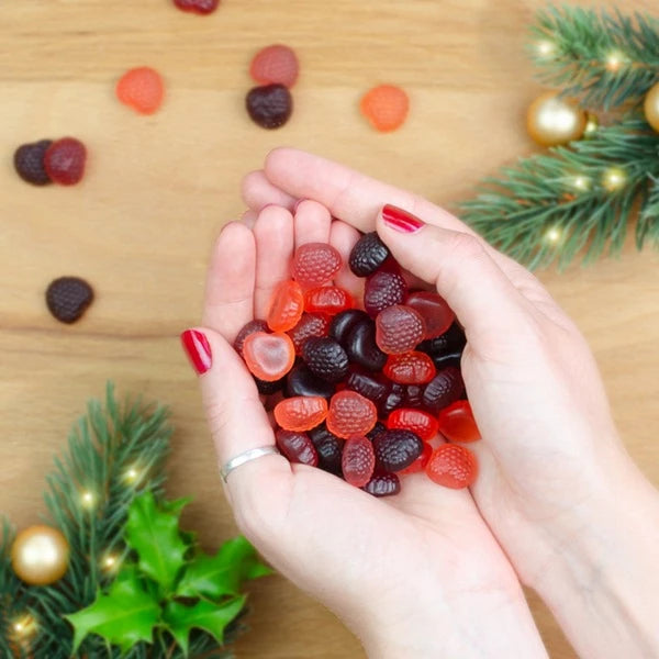 Hände mit rotem Nagellack halten Gummibärchen, winterliche Dekoration im Hintergrund.