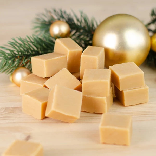 Stapel Karamellwürfel mit Tannenzweigen und Weihnachtskugeln im Hintergrund