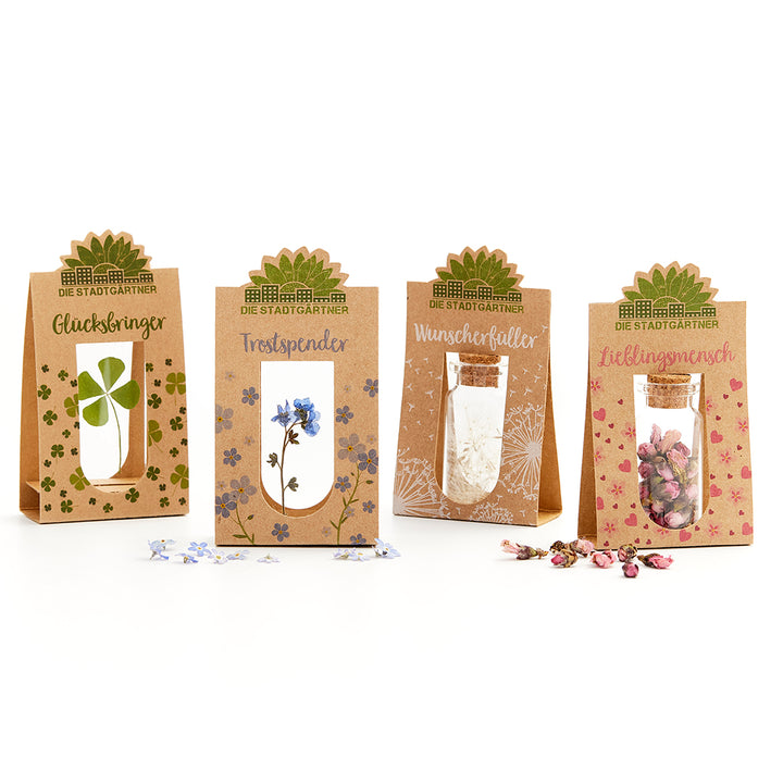 Vier Geschenkverpackungen von "Die Stadtgärtner" mit kleinen Gläsern und unterschiedlichen getrockneten Pflanzen sowie Beschriftungen: Glücksbringer, Trostspender, Wunscherfüller und Lieblingsmensch.