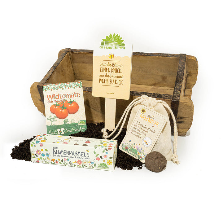 Gartenbau-Set mit Holzkiste, Saatguttüten, Erde und Samentabletten auf weißem Hintergrund.