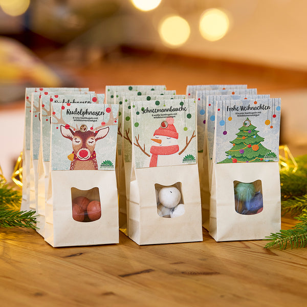Drei weihnachtlich dekorierte Tüten mit Süßigkeiten auf einem Holztisch, jeweils mit den Aufschriften „Rudolphnasen“, „Schneemannbäuche“ und „Frohe Weihnachten“.