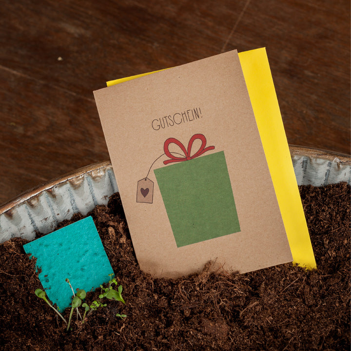 Gutschein-Karte mit Geschenk Illustration in Erde neben Jungpflanzen.
